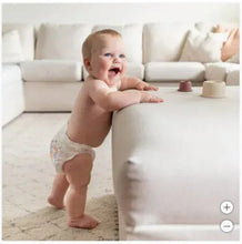 Toddler wearing a white diaper with light prints, standing on a living-room floor