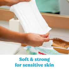 Hand pulling a white baby wipe from a HUGGIES fresh & clean wipe pack