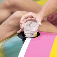 Hand holding a drink cup on inflatable island cup holder over pink and teal stripes