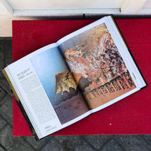 Hardcover illustrated book open, fantasy battle scene illustration with text on left page