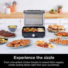 Indoor electric grill with open lid, showing multiple cooked foods on plates