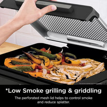 Indoor electric grill with lid open, cooking seafood and mixed vegetables on griddle