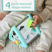 Child holding teal and white activity triangle shape sorter with green and orange shapes