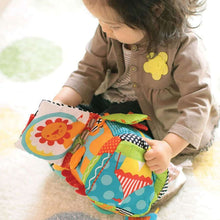 Plush activity cube with bright panels, busy straps, and a lion graphic; held by child