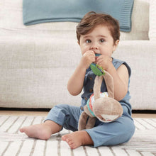 Baby holding plush sloth toy with tan head, colorful rings, and teal teether