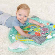 Baby lying on a narwhal-shaped teal tummy time play mat with colorful sea animals