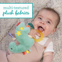 Baby chewing a yellow teether while holding a teal plush dinosaur with star patches.