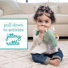 Baby holding teal plush dinosaur teether toy with dangling textures on a soft rug.