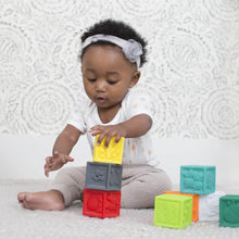 Baby reaching for multicolor cube plastic blocks with embossed patterns