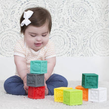 Baby playing with stack of multicolor cube plastic blocks with embossed details