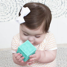 Baby holding teal plastic cube block with embossed pattern