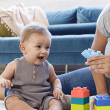 Baby playing with multicolor soft building blocks, held on a sofa