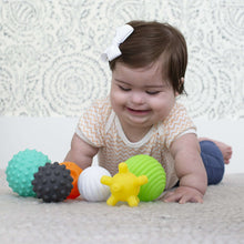 Baby playing with textured soft plastic balls in orange, teal, gray, white, green, and yellow