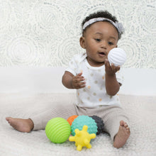Baby lying with textured soft plastic balls, including a white ridged ball and yellow star ball
