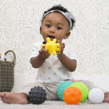 Baby playing with textured soft plastic balls, holding a yellow star-shaped ball