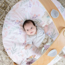 Round baby play mat with floral quilted top and dangling toy arch, baby lying on it