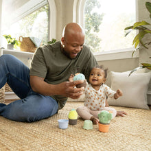 Nesting rattle set with stackable plush cups on the floor; green, teal, and orange