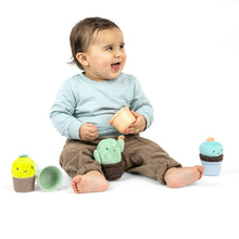 Baby playing with stackable nesting rattles; plush character cups in green, orange, teal
