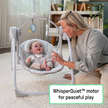 Baby seated in plush portable swing with caregiver nearby and hanging toy