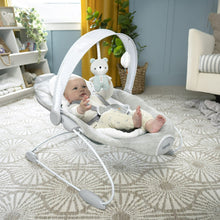 Automatic baby bouncer seat with attached toys, infant lying reclined on patterned rug