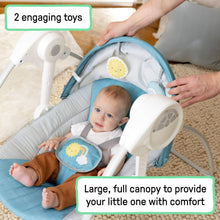 Baby resting in portable swing with large canopy and two hanging toys.