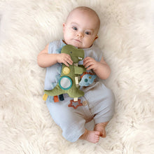 Olive green dino toy with teal circle ring and orange star clip in baby's hands
