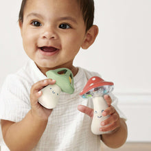 Toddler holding green and red mushroom musical rattles with smile faces and beads