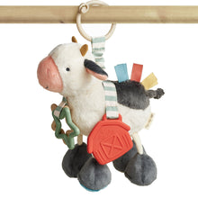 Plush cow activity toy with loop handle, red teether, and green link detail