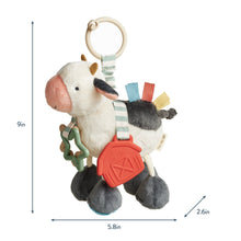 Plush cow activity toy with hanging ring, red teether, and striped fabric straps