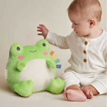 Green frog plush with multicolor ribbon tags as a baby reaches toward it