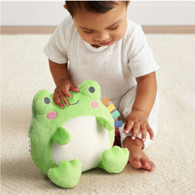 Green frog plush held by a child, smiling embroidered face and white belly