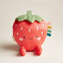 Plush strawberry toy with green leaf top, red body, stitched face, and multicolor ribbon tabs
