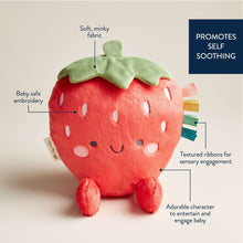 Plush strawberry toy with green leaf, soft red fabric, smiling face and sensory ribbon accents