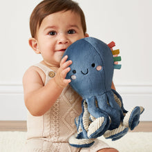Blue plush octopus held by a baby, with embroidered face and textured ribbon tentacles.