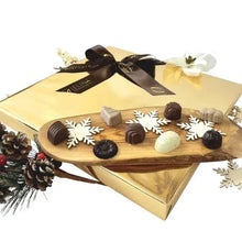 Assorted chocolates on a board atop a gold gift box with brown ribbon and snowflake accents