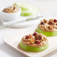 Peanut butter dollops on apple slices with chopped nuts on a serving board