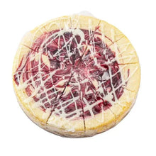 Round cheesecake with white drizzle, raspberry swirls, and chocolate shards