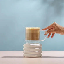 Fluted double-wall glass mug with amber coffee, hand gripping the clear handle