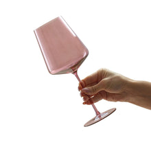 Pink tinted wine glass with red wine held in a hand, angled for pouring