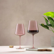 Two pink tinted wine glasses with red wine, slender stems and round bases