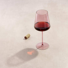Pink tinted wine glass with red wine, shown upright
