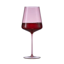Single pink tinted wine glass with red wine, wide rim and slender base