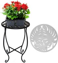 Black round metal plant stand with decorative cutout top and four scroll legs.