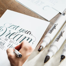 Fine line ink pens with black nibs in use for lettering on paper