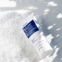 Foaming cream cleanser tube with blue label, surrounded by foamy water bubbles