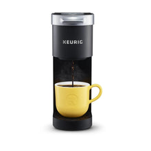 Black Keurig K-Mini single serve coffee maker pouring into yellow mug