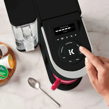 Coffee maker touchscreen and dial with finger pressing, with red mug beneath