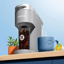 Gray Keurig K-Iced coffee maker pouring over iced coffee with blue mug