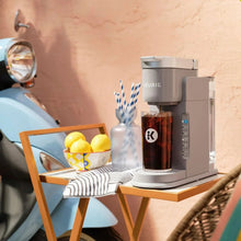 Gray Keurig K-Iced single-serve coffee maker dispensing iced coffee with blue mug