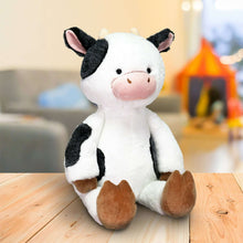 Plush cow stuffed animal sitting, white fur with black patches and brown hooves